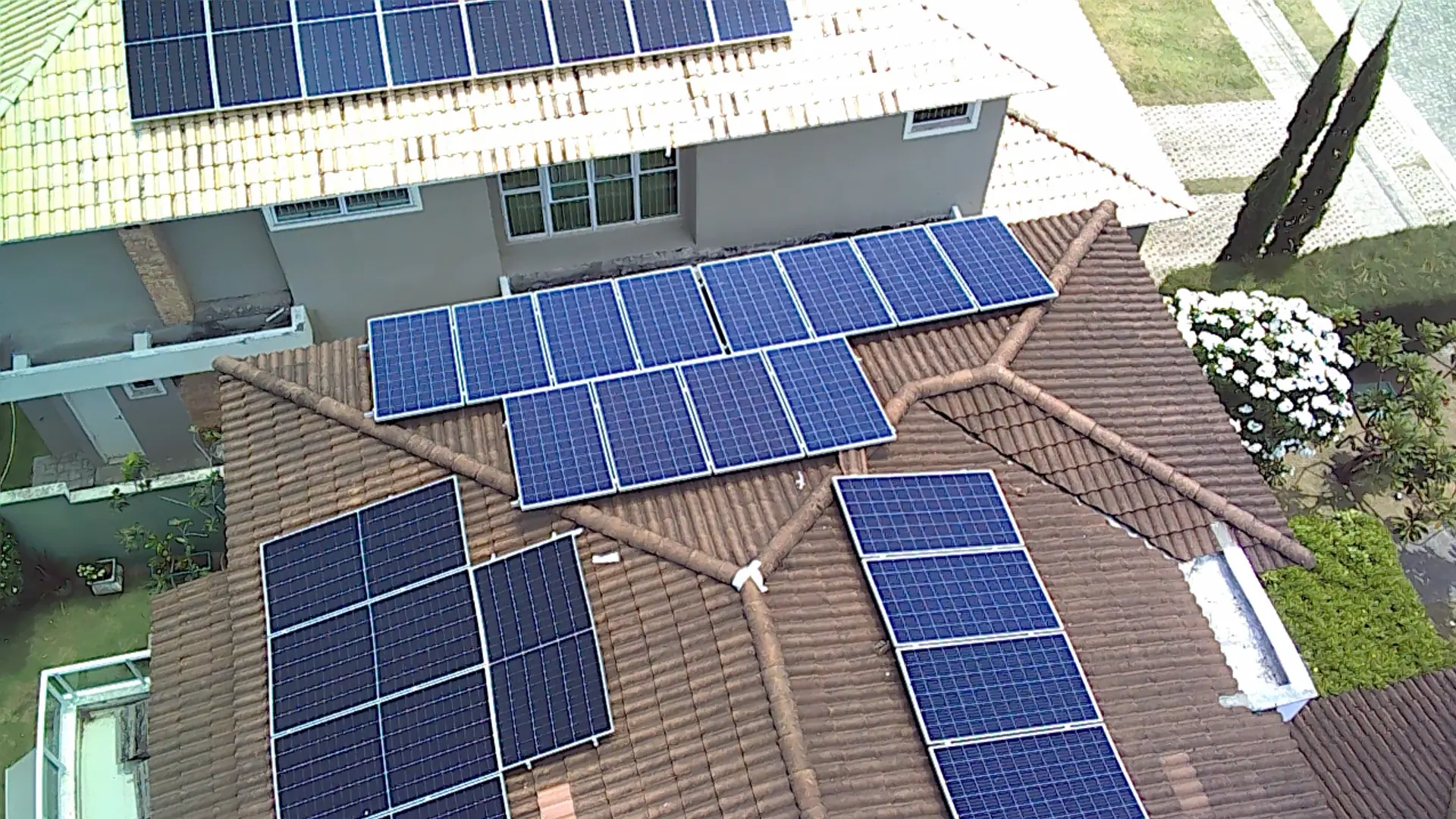 Vista aérea de módulos fotovoltaicos instalados no telhado de uma residência com piscina